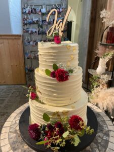 Elegante mehrstöckige Hochzeitstorte in weiß mit goldenen Details und frischen Blumen handgeamcht im Muehlviertel